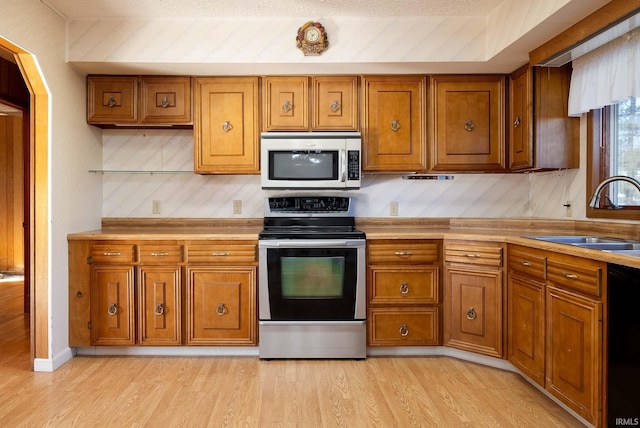 kitchen with appliances with stainless steel finishes, sink, and light hardwood / wood-style flooring