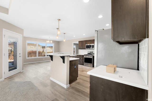 kitchen featuring appliances with stainless steel finishes, a breakfast bar, hanging light fixtures, dark brown cabinetry, and a center island with sink