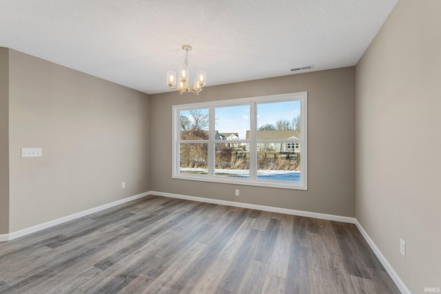 spare room featuring dark hardwood / wood-style flooring, a textured ceiling, and a chandelier