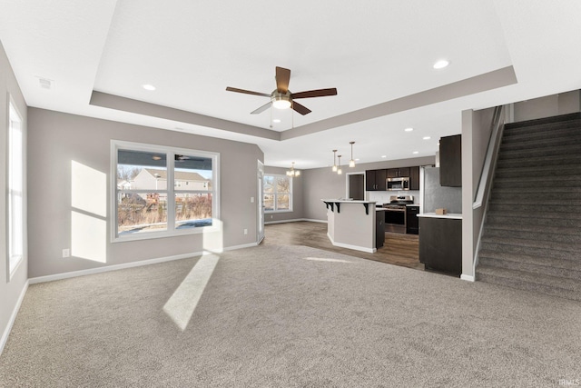 unfurnished living room with dark carpet, a tray ceiling, and ceiling fan with notable chandelier