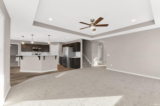 unfurnished living room with ceiling fan, a raised ceiling, and carpet floors