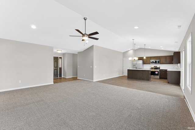 unfurnished living room with ceiling fan with notable chandelier, carpet floors, and vaulted ceiling