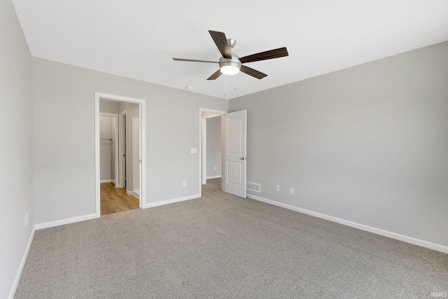 unfurnished bedroom with a spacious closet, light carpet, and ceiling fan