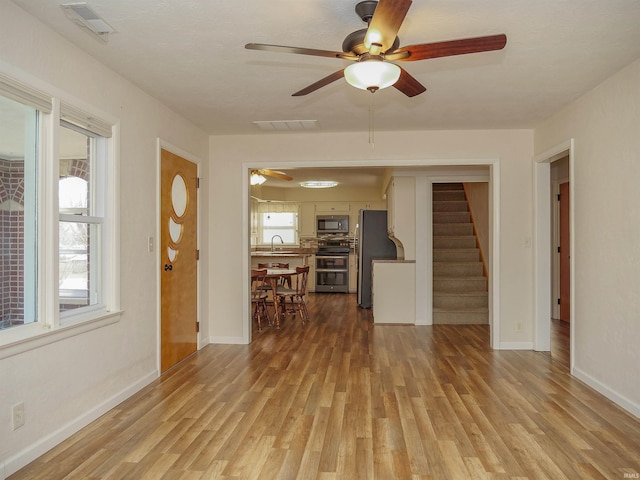 unfurnished living room featuring ceiling fan, sink, a wealth of natural light, and light wood-type flooring