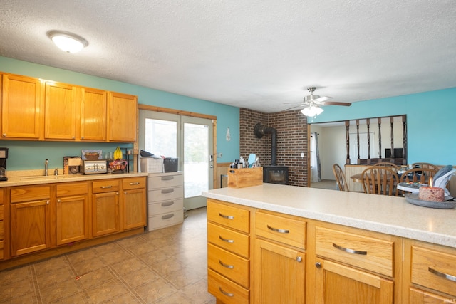 kitchen with ceiling fan, a wood stove, sink, and a textured ceiling