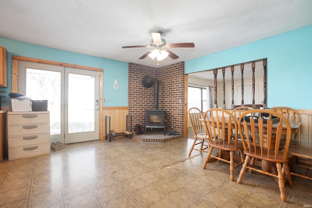 dining area with ceiling fan, wooden walls, a textured ceiling, and a wood stove