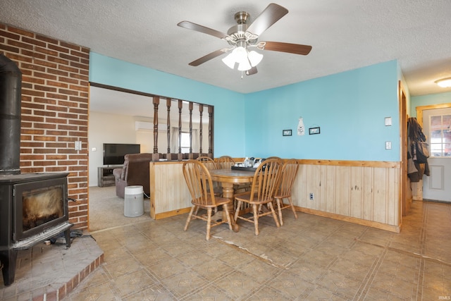 dining room featuring ceiling fan, wooden walls, a textured ceiling, and a wood stove