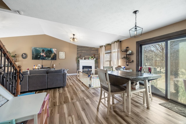 dining area featuring hardwood / wood-style flooring, wooden walls, a large fireplace, a textured ceiling, and vaulted ceiling