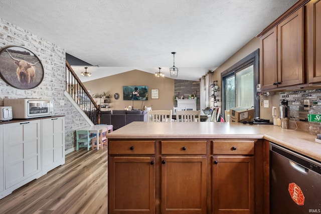 kitchen with vaulted ceiling, pendant lighting, stainless steel dishwasher, and kitchen peninsula