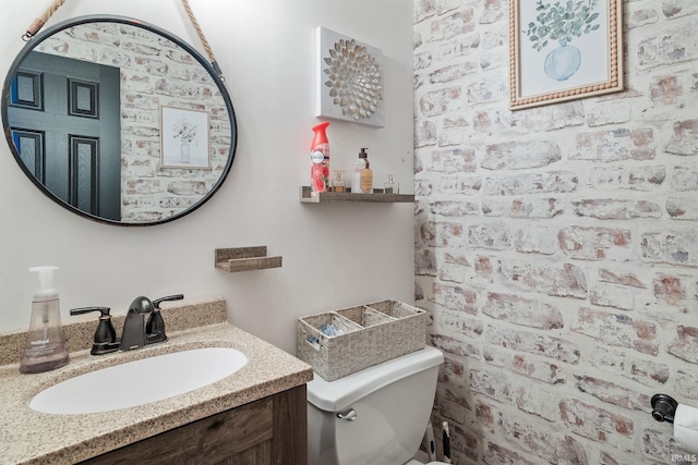 bathroom featuring vanity, brick wall, and toilet