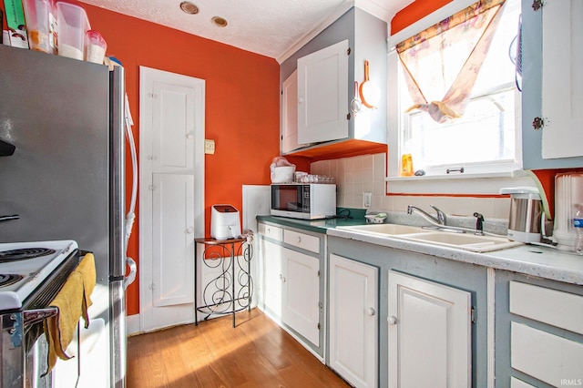 kitchen with sink, tasteful backsplash, white cabinetry, light hardwood / wood-style flooring, and appliances with stainless steel finishes