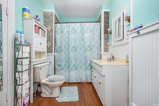 bathroom with curtained shower, wood-type flooring, vanity, toilet, and a textured ceiling