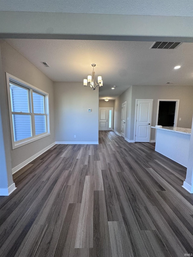 unfurnished living room with baseboards, visible vents, dark wood-style floors, and an inviting chandelier