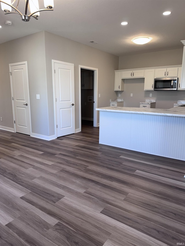 kitchen with an inviting chandelier, dark wood finished floors, stainless steel microwave, and white cabinets
