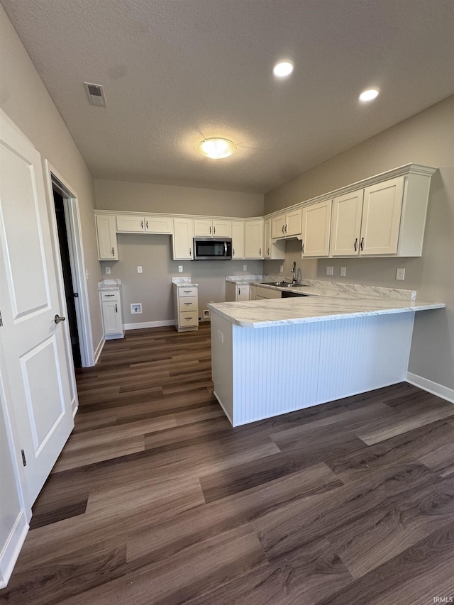 kitchen with white cabinets, a peninsula, stainless steel microwave, and baseboards