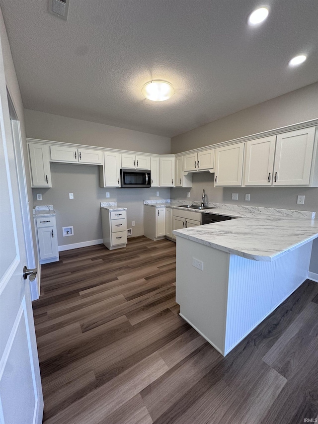 kitchen featuring a peninsula, white cabinetry, stainless steel microwave, and dark wood-style floors