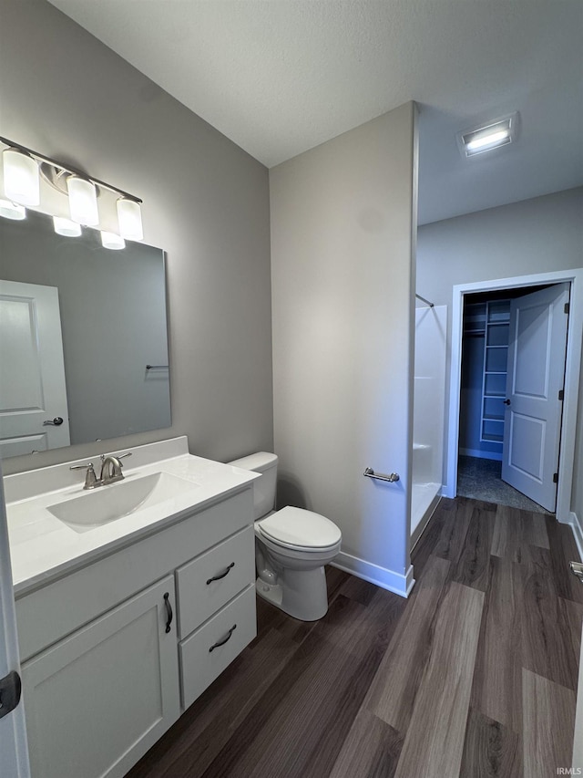 bathroom featuring vanity, wood finished floors, toilet, baseboards, and walk in shower