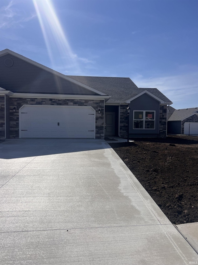 ranch-style house featuring an attached garage, stone siding, and concrete driveway