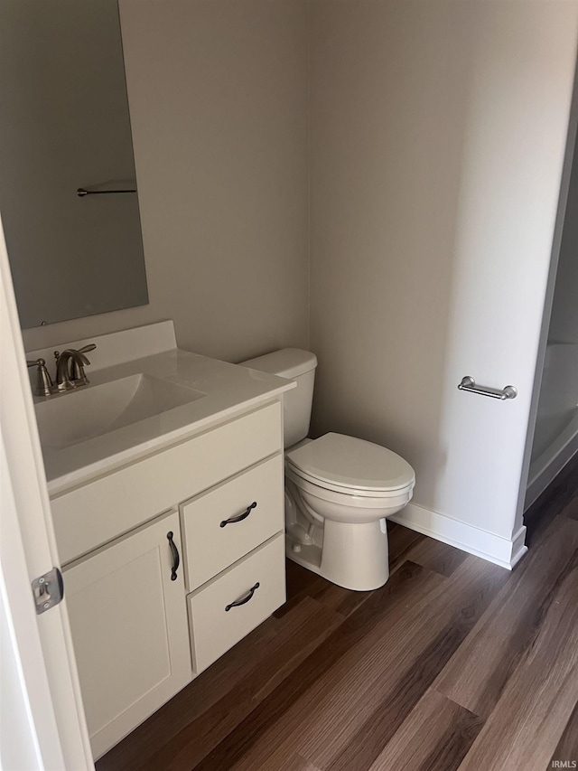 bathroom featuring toilet, baseboards, wood finished floors, and vanity