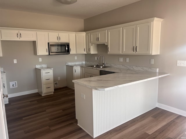 kitchen with dark wood finished floors, a sink, light countertops, stainless steel microwave, and a peninsula