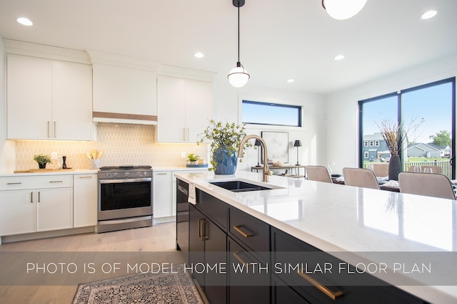 kitchen with sink, stainless steel gas range oven, white cabinetry, decorative light fixtures, and plenty of natural light