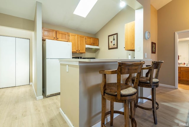 kitchen with light wood-type flooring, a kitchen breakfast bar, kitchen peninsula, and white fridge