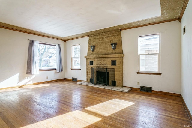 unfurnished living room featuring crown molding, a stone fireplace, wood-type flooring, and plenty of natural light