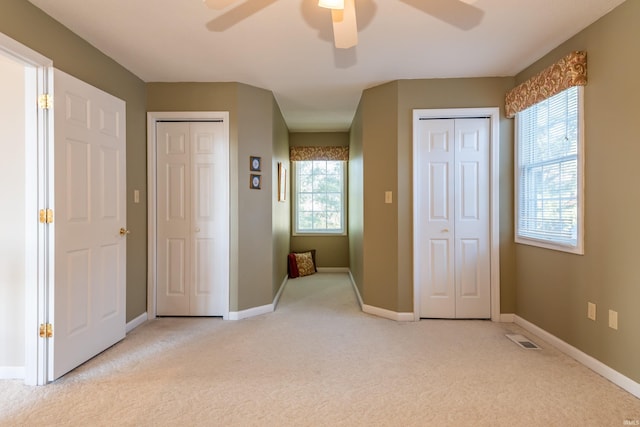 unfurnished bedroom with ceiling fan, light colored carpet, multiple windows, and two closets