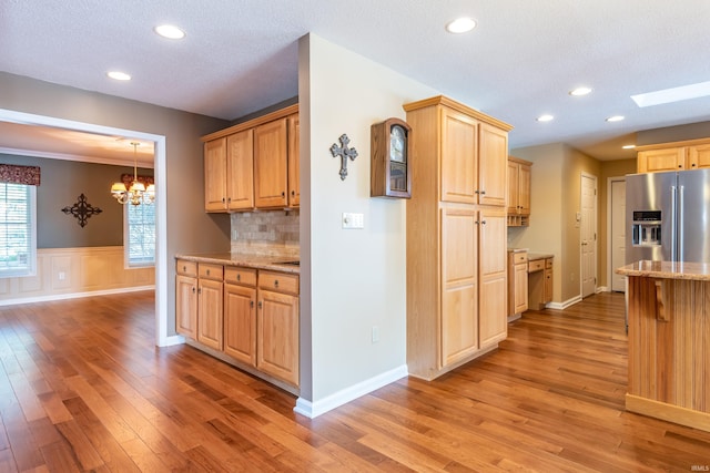 kitchen with a skylight, tasteful backsplash, hardwood / wood-style flooring, light stone counters, and stainless steel refrigerator with ice dispenser