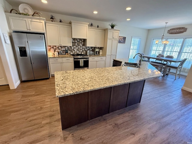 kitchen featuring sink, decorative light fixtures, a center island with sink, light wood-type flooring, and appliances with stainless steel finishes