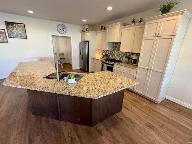 kitchen featuring appliances with stainless steel finishes, sink, backsplash, light stone counters, and a center island with sink