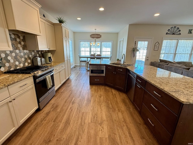 kitchen featuring dark brown cabinetry, sink, decorative light fixtures, stainless steel appliances, and light hardwood / wood-style floors