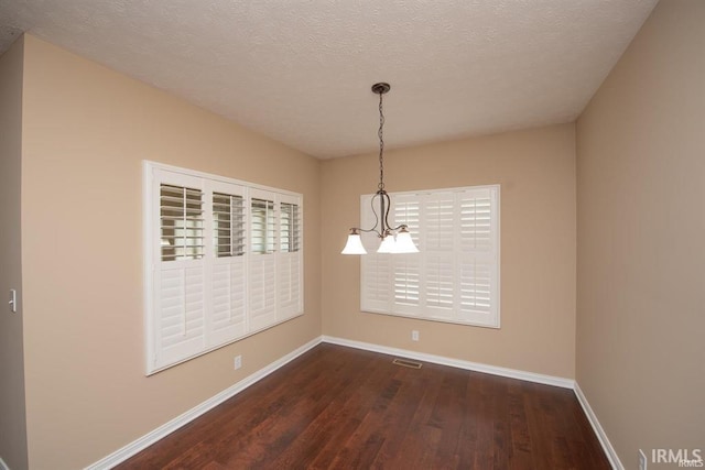 unfurnished dining area featuring a textured ceiling, dark hardwood / wood-style floors, and a chandelier