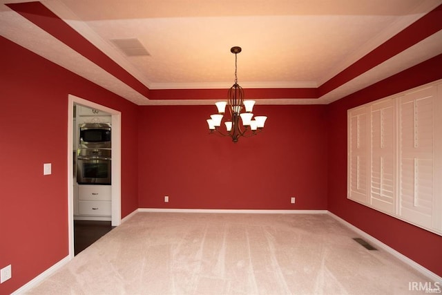 carpeted empty room featuring an inviting chandelier, ornamental molding, and a tray ceiling