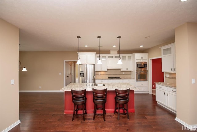 kitchen with appliances with stainless steel finishes, sink, white cabinets, a kitchen island with sink, and light stone countertops