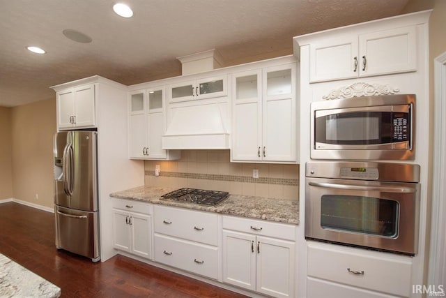 kitchen with dark wood-type flooring, appliances with stainless steel finishes, light stone countertops, white cabinets, and decorative backsplash