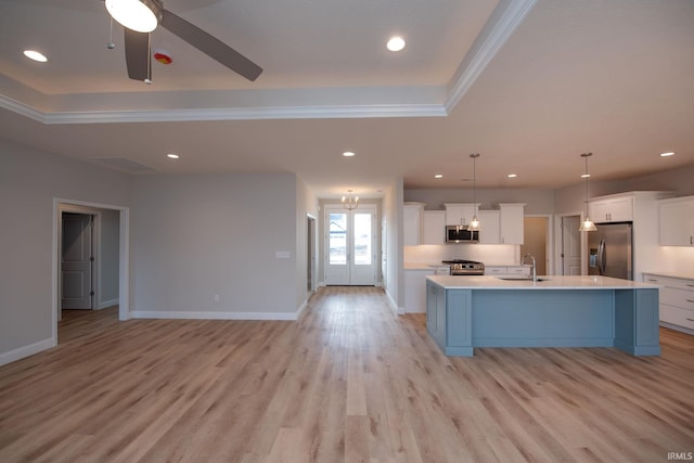 kitchen featuring hanging light fixtures, stainless steel appliances, a tray ceiling, white cabinets, and a center island with sink