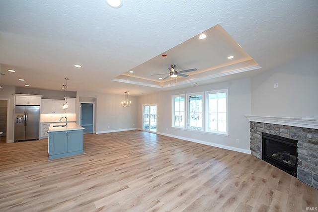 unfurnished living room with sink, a stone fireplace, a raised ceiling, and light wood-type flooring