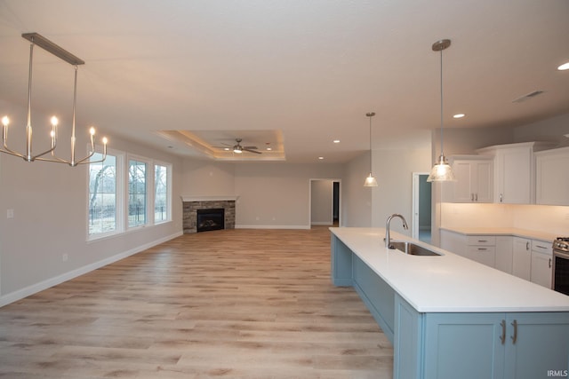 kitchen featuring sink, white cabinetry, decorative light fixtures, a center island with sink, and a tray ceiling