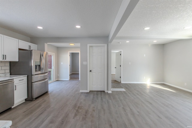 kitchen featuring white cabinetry, light wood-type flooring, backsplash, stainless steel appliances, and a textured ceiling