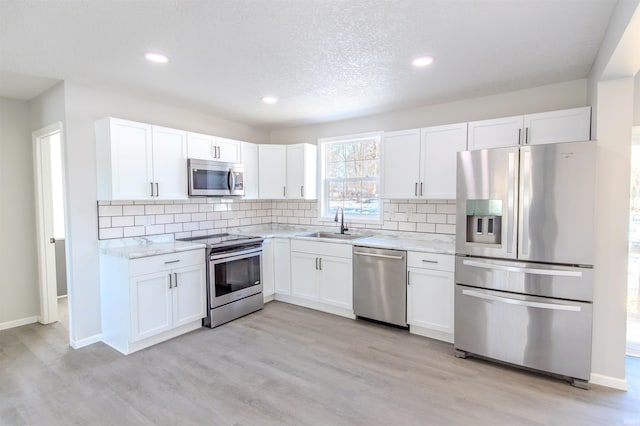 kitchen with sink, appliances with stainless steel finishes, white cabinetry, light hardwood / wood-style floors, and light stone countertops