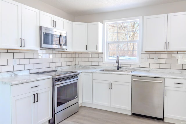 kitchen with sink, light stone counters, tasteful backsplash, appliances with stainless steel finishes, and white cabinets