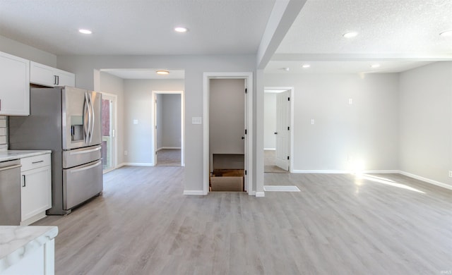 kitchen featuring white cabinetry, light stone counters, a textured ceiling, appliances with stainless steel finishes, and light hardwood / wood-style floors