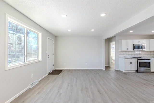 unfurnished living room with a healthy amount of sunlight, a textured ceiling, and light wood-type flooring