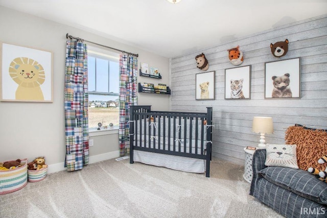 bedroom featuring multiple windows, carpet floors, a crib, and wooden walls