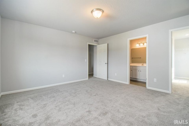 unfurnished bedroom featuring light colored carpet, ensuite bathroom, a spacious closet, and a closet