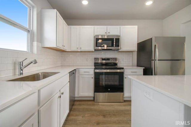 kitchen with sink, tasteful backsplash, wood-type flooring, stainless steel appliances, and white cabinets