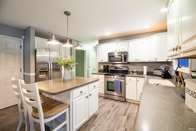 kitchen featuring hanging light fixtures, appliances with stainless steel finishes, white cabinets, and light wood-type flooring