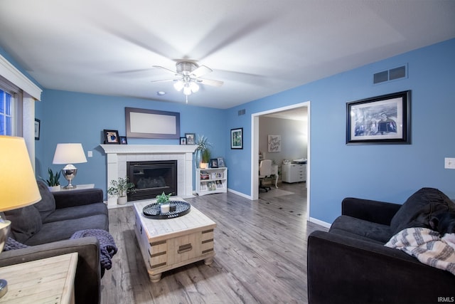 living room featuring a tile fireplace, hardwood / wood-style floors, and ceiling fan