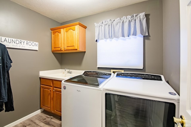 laundry room with sink, light hardwood / wood-style flooring, cabinets, washer and dryer, and a textured ceiling